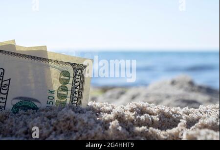 Trois billets de dollars sont enterrés dans le sable sur la plage de sable près de la mer sous le soleil Banque D'Images