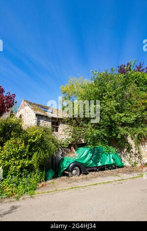 Vieille voiture couverte de bâche verte devant un chalet en pierre près de Hexham Northumberland Banque D'Images