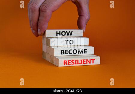 Comment devenir un symbole résilient. Concept de mots 'Comment devenir résilient' sur des blocs de bois sur un magnifique fond orange. Main d'homme d'affaires. Entreprise, Banque D'Images