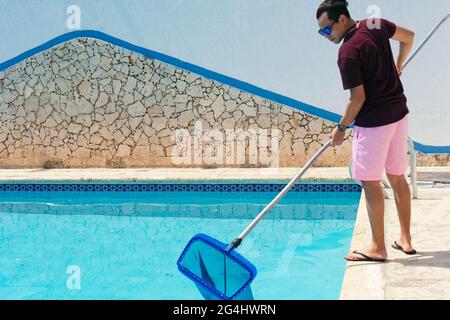 Homme nettoyant piscine de feuilles mortes avec filet en été Banque D'Images