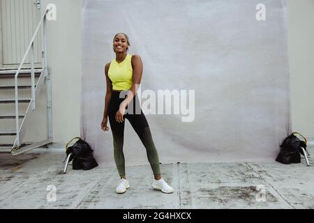 Portrait complet d'une femme en vêtements de sport se détendant après l'entraînement sur le toit. Femme de fitness africaine debout sur la terrasse du bâtiment regardant la caméra et Banque D'Images