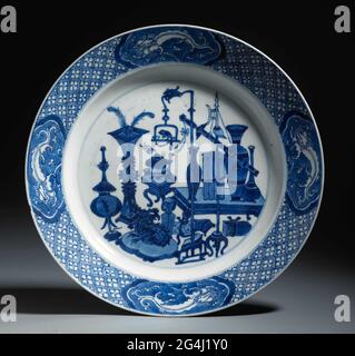 . Plaque en porcelaine, peinte en bleu sous-brillant. Sur les antiquités plates (vases, plumes de paon, livres, rouleaux, brûleur de flock) et les objets merveilleux tels qu'une photo d'un dragon sur un oreiller et d'un perroquet sur la norme; le bord avec serviette entrélé avec des cartouilles de hall avec un dragon en blanc enregistré sur un fond bleu; Sur le dos des valeurs (diamant, perle, pierre musicale), des symboles chanceux (coquille) et un attribut des huit immortels (calanges). Sur le dessous, un repère de joint est marqué d'un double cercle. Deux éclats et une fissure dans le bord. Bleu blanc. Banque D'Images