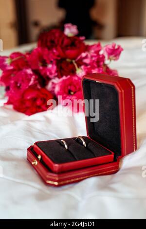 Deux anneaux de mariage en or sur le fond d'un bouquet de mariage, dans une boîte rouge. Vacances. Fleurs roses. Banque D'Images