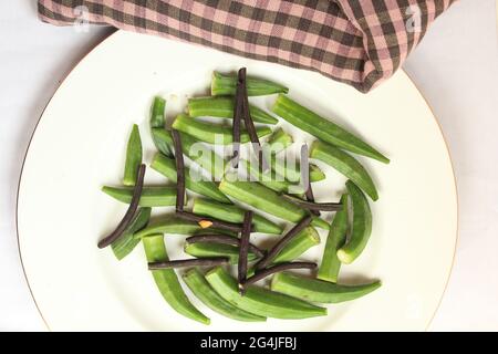 Vue en grand angle de la pile d'okra vert frais sur plaque blanche isolée sur fond blanc. Légumes et plantes sains. Ingrédients de cuisine courants au Bangladesh. Banque D'Images