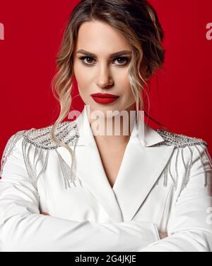 Portrait de femme blonde arrogante avec maquillage permanent parfait en blouson blanc avec pattes aux épaules, bras croisés à la poitrine Banque D'Images