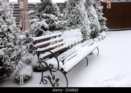 Banc couvert de neige dans la cour d'une maison par une journée d'hiver nuageux Banque D'Images