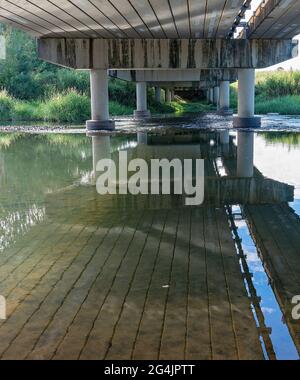 Sous un pont en béton construit au-dessus d'un ruisseau rural peu profond avec des reflets d'eau Banque D'Images