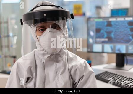 Portrait d'un scientifique fatigué en coverall regardant l'appareil photo assis dans un laboratoire moderne équipé. Équipe de scientifiques examinant l'évolution du virus à l'aide d'outils de haute technologie et de chimie pour la recherche scientifique, le développement de vaccins. Banque D'Images