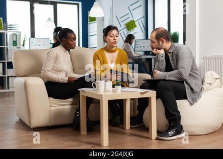 Des hommes d'affaires multiethniques se sont concentrés à lire le rapport financier annuel d'une tablette assise sur un canapé dans un bureau d'affaires moderne. Équipe diversifiée d'hommes d'affaires multiethniques travaillant en entreprise Banque D'Images