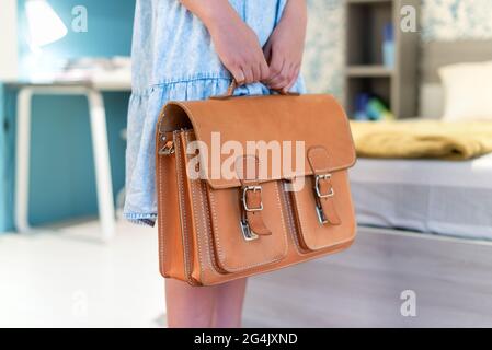 Fille tenant un sac d'école classique en cuir dans sa chambre dans une vue rapprochée Banque D'Images