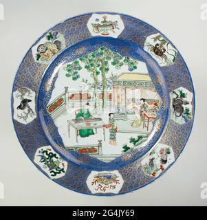 . Plat en porcelaine avec paroi surélevée et bord incliné, peint en bleu sous-glaçure et sur le bleu glaçure, rouge, vert, jaune, aubergine, noir et or. Le devant du plat est couvert de bleu clair poudré (bleu poudré) avec hangar sur le plat une grande réserve avec bord festonné rempli de trois personnes sur une terrasse clôturée avec des rochers et deux arbres, un érudit à une table jouant sur un Qin, Une dame assise à une table pour un lit, une femme de ménage avec un bol sur un plateau; le mur avec une décoration dorée sur le bleu avec des rosettes de farine et des tendrils; le bord avec une décoration dorée sur le bleu avec un motif géométrique, la clarifie Banque D'Images