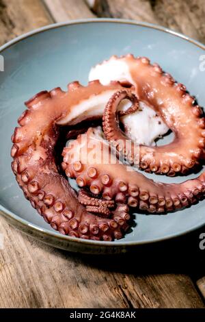 Tentacules cococalées de poulpe sur plaque de céramique bleue sur fond de bois brun. Gros plan Banque D'Images