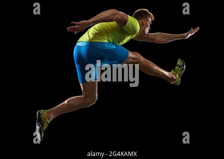 Athlète homme athlète saute au-dessus de la barrière isolée sur fond noir. Banque D'Images