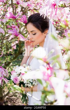 Jeune mariée en voile debout près du magnolia en fleurs Banque D'Images