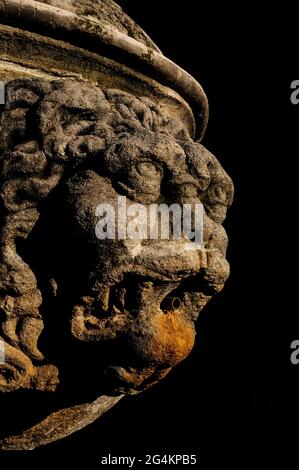 Fin décembre Sunshine ramasse les détails sculpturaux et la texture de ce visage grotesque, semi-humain mais limoneux, un mascaron ou masque en pierre qui se dresse au milieu des ombres profondes de la fontaine du début du XVIIIe siècle sur la place Saint-Siffrein à Carpentras, Vaucluse, Provence-Alpes-Côte d'Azur, France. La fontaine se dresse avant la porte gothique flamboyant des Juifs (porte juive) du début du XVIe siècle, portail sud de l'ancienne Cathédrale Saint-Siffrein. Il a été construit parmi plusieurs pour distribuer l'eau propre abondante apporté par un aqueduc construit en 1734. Banque D'Images