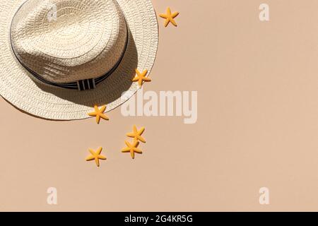 chapeau en osier blanc de paille sur fond de sable couleur avec vue sur le dessus des étoiles de mer jaunes. ombres dures du soleil. concept minimal de voyage et de vacances avec esprit Banque D'Images
