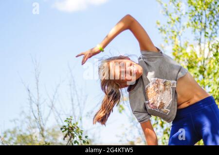 Défocus préadolescence caucasienne faire de l'exercice physique dans le parc, la forêt, à l'extérieur, à l'extérieur. Estomac mince. Bien-être sain style de vie. Exercice de pliage latéral Banque D'Images