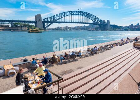 Les gens dînant et buvant un café près du port de Sydney et de l'Opéra de Sydney au soleil de midi d'avril en Nouvelle-Galles du Sud, en Australie Banque D'Images