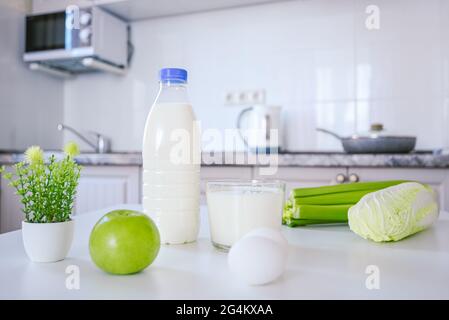 produits biologiques de la ferme de lait blanc protéines sur la table de cuisine une bouteille de lait et une tasse. oeufs vert céleri pomme napa chou Banque D'Images