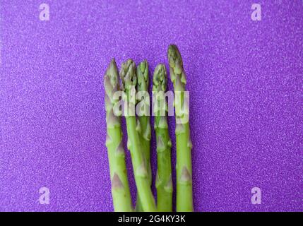 Gros plan sur un bouquet d'asperges fraîches sur fond violet scintillant Banque D'Images