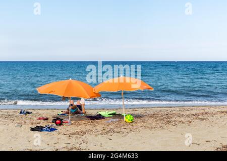 Personne se reposant sous deux parasols orange sur la plage de Prunete. Corse, France Banque D'Images