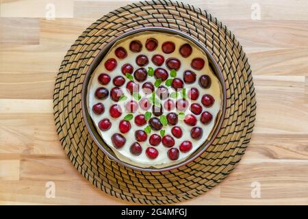 Le cheesecake maison est recouvert de cerises fraîches et d'une branche de menthe dans un moule à gâteau rond sur une table en bois Banque D'Images