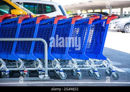 Les chariots bleus sont empilés dans une rangée dans le stationnement d'un supermarché, avec des voitures défocassées à l'arrière-plan Banque D'Images