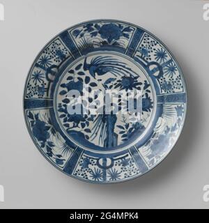 Plat avec deux Hoo-Birds Near Rocks et plantes à fleurs. Plat en porcelaine, peint en bleu sous-brillant. Sur le plat dans un double médaillon un oiseau de foin sur une roche dans les plantes en fleurs (pivoine, grenade). Un deuxième oiseau survole. Le bord est divisé en parcours larges et étroits. Les grands sujets avec plantes à fleurs (pivoine, prunus, camélia) aux rochers; les cours étroits avec une boisson de fleur. Cinq préen en bas. La décoration est basée sur la porcelaine d'écureuil chinois. Bleu blanc. Banque D'Images