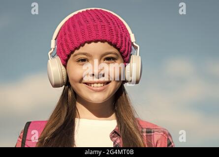 Protégez vos oreilles pour enfants. Bonne fille porte des écouteurs sur ciel bleu ensoleillé. Un petit enfant écoute de la musique dans un casque. Soins de l'oreille et de l'ouïe. La vie moderne Banque D'Images