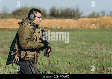 armé jeune homme blanc en uniforme militaire portant des écouteurs et des lunettes sur le terrain d'entraînement Banque D'Images