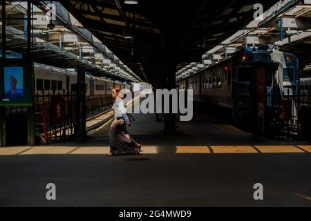Hoboken, NJ, États-Unis — 19 juin 2021. Une femme aux cheveux rouges marche à la hâte à travers une série de lumière dans la gare de Hoboken dans le New Jersey. Banque D'Images