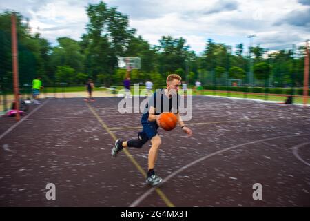 Jeune homme à tête rouge courant et dribbling un ballon de basket à grande vitesse sur un terrain de sport dans la rue pendant la journée le mouvement flou Banque D'Images