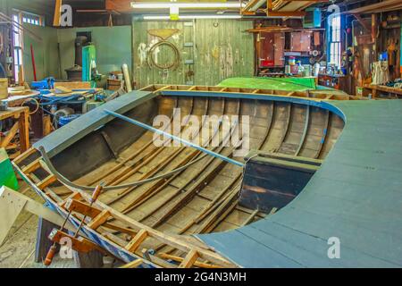 Bateau en bois partiellement construit dans un ancien atelier de marina sombre avec des lumières fluorescentes - mise au point sélective et lumière vive éblouissante dans les fenêtres Banque D'Images