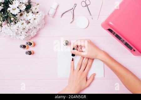 Les mains des femmes appliquent du gel vernis à ongles pendant la procédure de manucure à la maison sur la table rose, vue de dessus. Banque D'Images