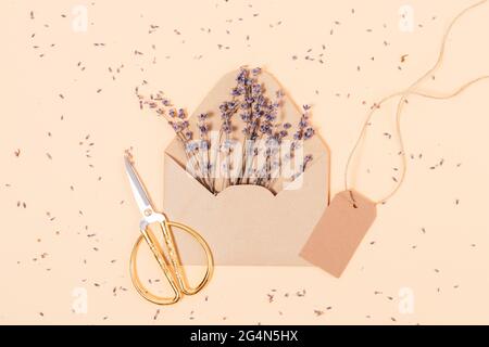 Vue de dessus enveloppe marron avec fleurs de lavande et ciseaux sur fond beige. Banque D'Images