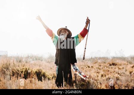 rastafari ethnique ancien gai avec des dreadlocks regardant loin célébrer la victoire tout en se tenant dans un pré sec dans la nature Banque D'Images