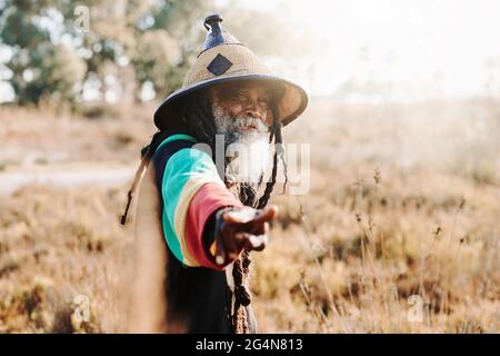 rastafari ethnique ancien gai avec des dreadlocks regardant l'appareil-photo dans un pré sec dans la nature Banque D'Images