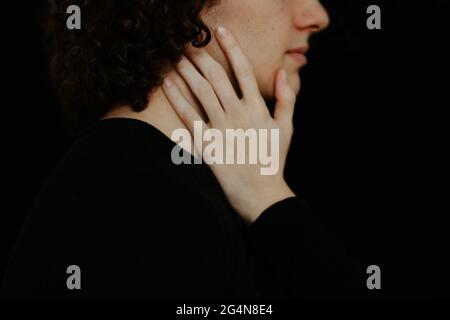 Vue latérale de la petite amie touchant doucement le visage d'un petit ami méconnaissable sur fond noir en studio Banque D'Images