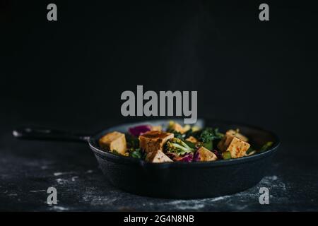 Salade végétarienne avec tofu frit et légumes servis sur fond noir Banque D'Images