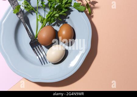 Vue de dessus des œufs de poulet sur l'assiette avec fourchette contre les brins de persil frais sur fond de deux couleurs Banque D'Images