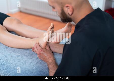 Homme barbu médecin examinant le pied de récolte anonyme femme sur la table pendant la physiothérapie en clinique Banque D'Images