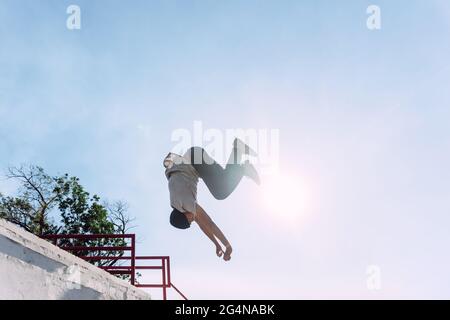 Jeune homme intrépide et bas angle sautant au-dessus de la rampe métallique en ville tout en effectuant un spectacle de cascades par temps ensoleillé Banque D'Images