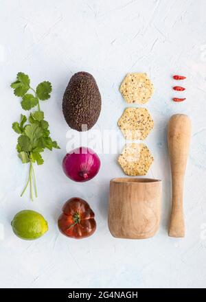 Vue de dessus avec Haas avocat et tomates avec légumes frais et mortier en bois pour cuisiner guacamole sur une surface blanche Banque D'Images