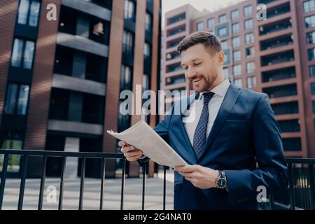 Un jeune économiste réussi et heureux lit dans le journal du matin un article contenant des informations financières Banque D'Images