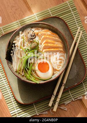 De la soupe de ramen de poulet dans un bol avec des baguettes sur une table en bois Banque D'Images