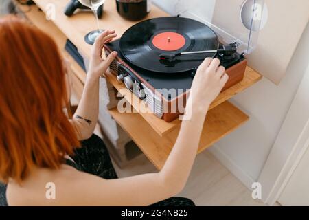 Vue du dessus de la récolte anonyme femelle tournant sur le lecteur de disques rétro sur l'étagère dans la maison Banque D'Images