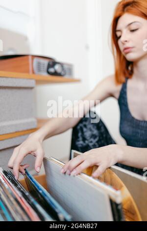 Jeune femme sélectionnant le disque en vinyle dans un conteneur en bois tout en étant assise contre la plaque tournante d'époque dans la chambre Banque D'Images