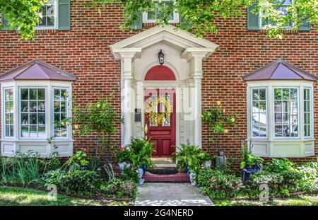 Entrée avec colonnes et baies vitrées d'une belle maison en briques de deux étages avec pots de fleurs et roses grimpantes jaunes et jardinières et fougères Banque D'Images