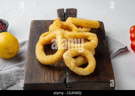 Rondelles d'oignon ou de calmars frits croquants dans un ensemble de pâte, sur le plateau de service, sur fond de table en pierre blanche Banque D'Images