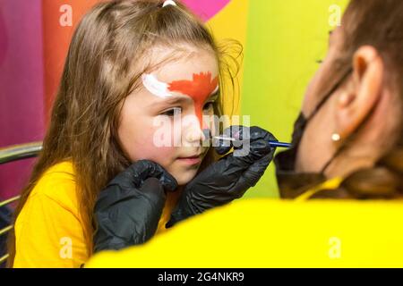 La fille peint le visage de la peinture sur le visage de la fille. Banque D'Images